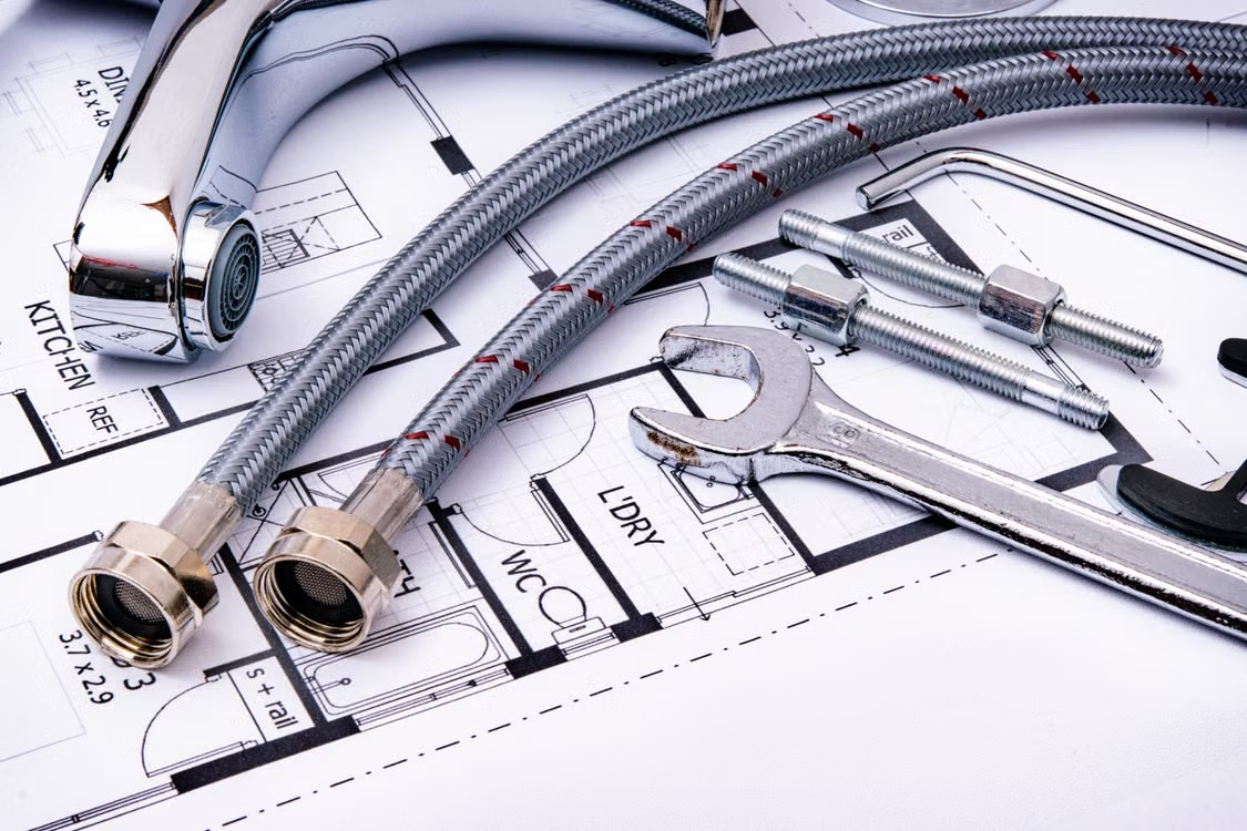 Plumbing tools and faucet placed over a residential plumbing blueprint.