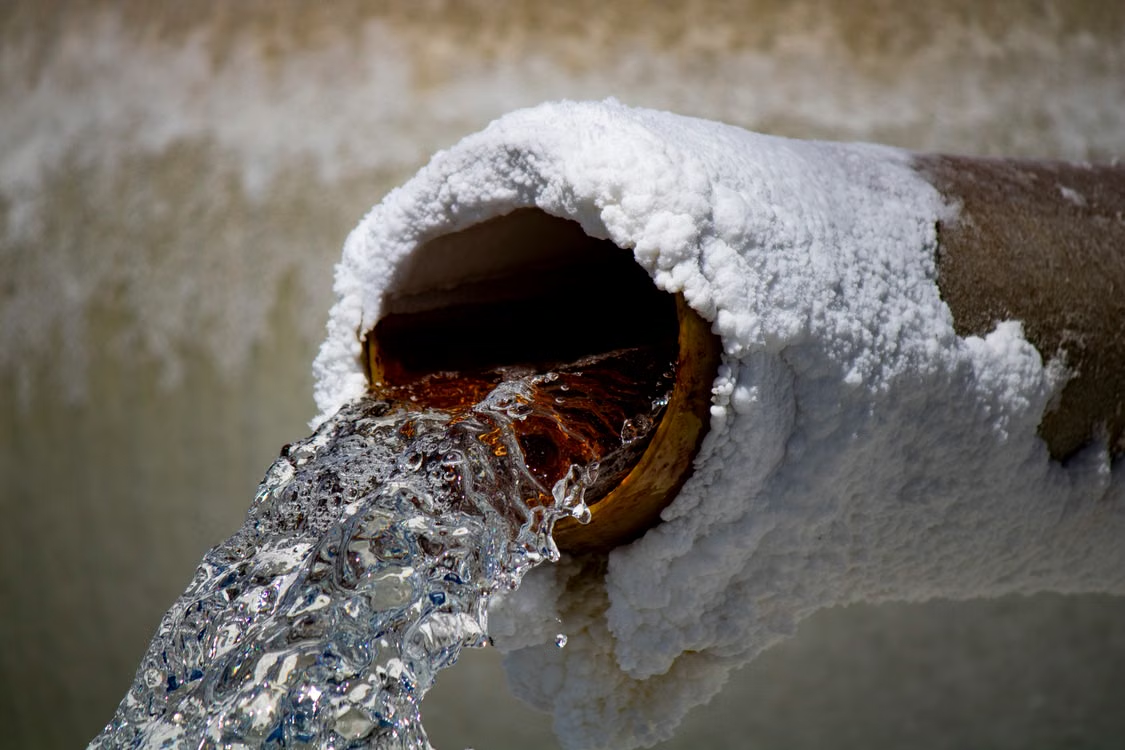 Water flowing from a rusty pipe with visible mineral and salt deposits.